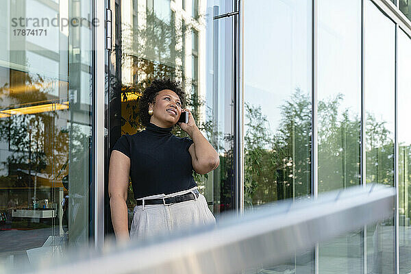 Junge Geschäftsfrau spricht mit Smartphone vor Glaswand