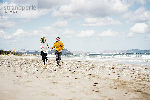 Fröhliches reifes Paar hält Händchen beim Laufen am Strand