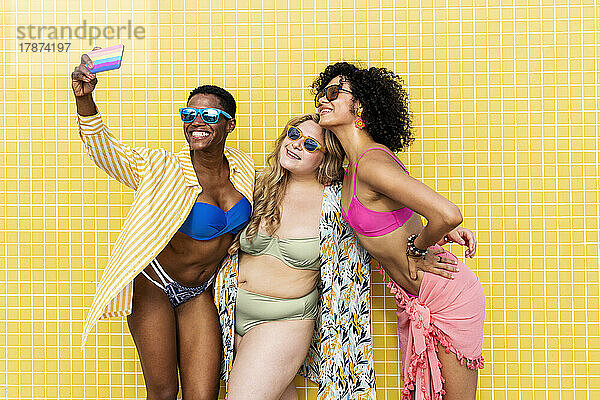 Fröhliche Freunde machen Selfie mit dem Smartphone in der gelben Wand