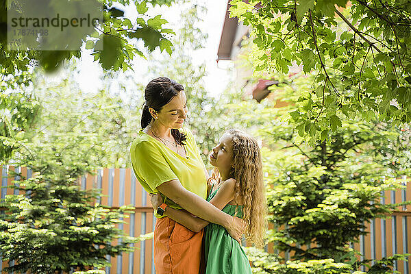 Lächelnde Frau umarmt Tochter im Hinterhof