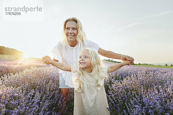 Cute girl with arms outstretched standing in front of mother at lavender field