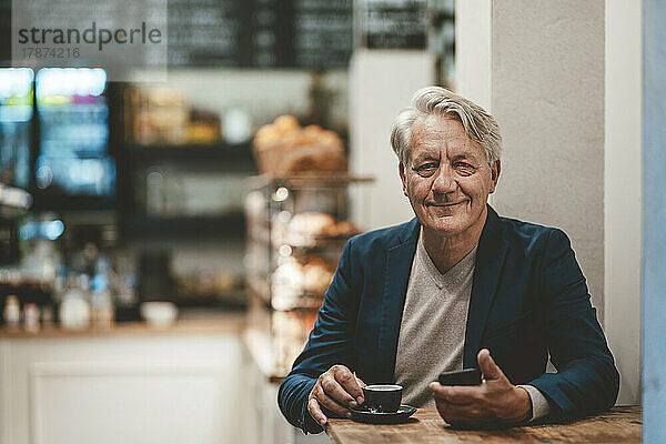 Lächelnder Geschäftsmann mit Kaffee auf dem Tisch im Café