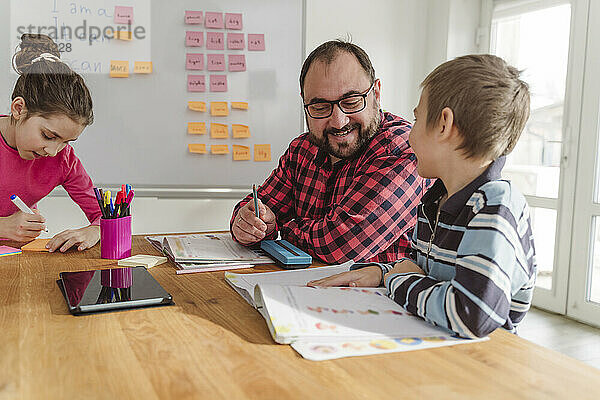 Lächelnder Nachhilfelehrer unterrichtet Jungen mit Buch am Tisch