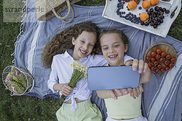 Smiling sisters taking selfie lying on picnic blanket