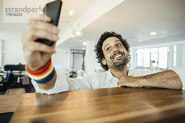 Lächelnder Geschäftsmann  der im Büro ein Selfie mit dem Mobiltelefon macht