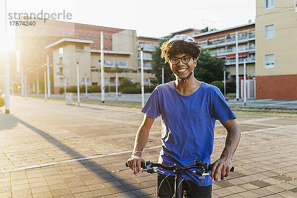 Glücklicher Mann mit Helm steht mit Fahrrad in der Stadt