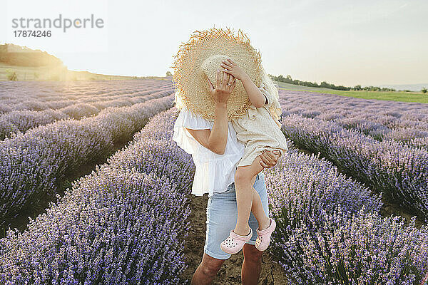 Mother and daughter covering face with hat in lavender field