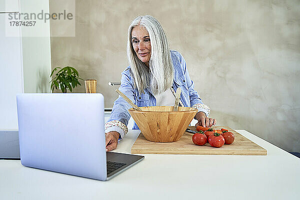 Frau mit Tomaten benutzt Laptop in der Küche