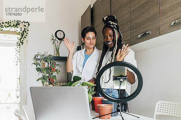 Lächelnde Frau mit Freundin filmt zu Hause Tutorial zur Pflanzenpflege