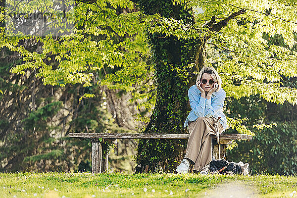 Reife Frau mit Sonnenbrille sitzt mit dem Kopf in den Händen auf einer Bank im Park