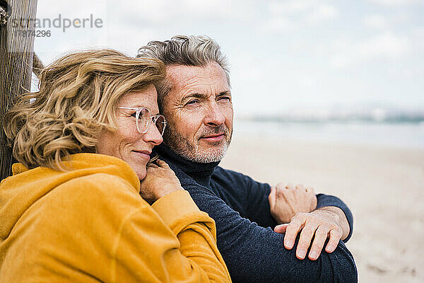 Lächelnde reife Frau mit Brille genießt den Urlaub mit Mann am Strand