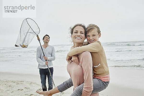 Sorglose Familie mit tragender Tochter  die am Strand spazieren geht  Vater mit Fischernetz
