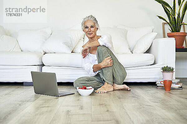 Frau mit Laptop und Schüssel Erdbeeren zu Hause