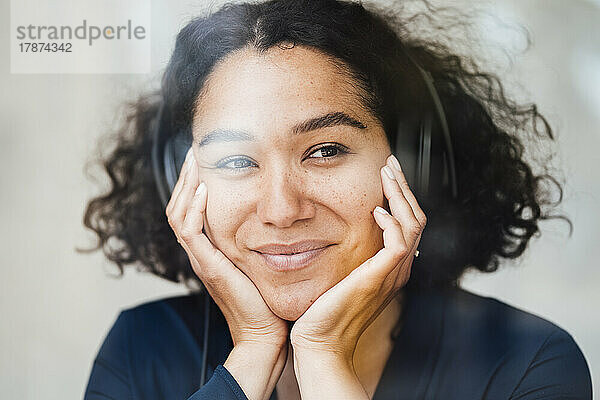 Lächelnde Frau  die über Kopfhörer Musik hört und durch Glas gesehen wird