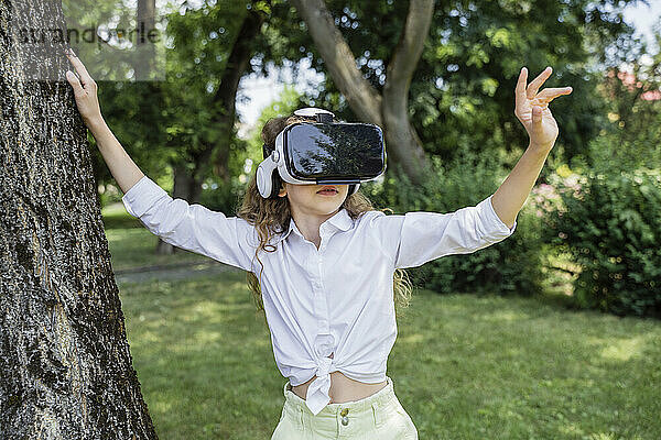 Mädchen mit Virtual-Reality-Simulator steht neben Baum im Park