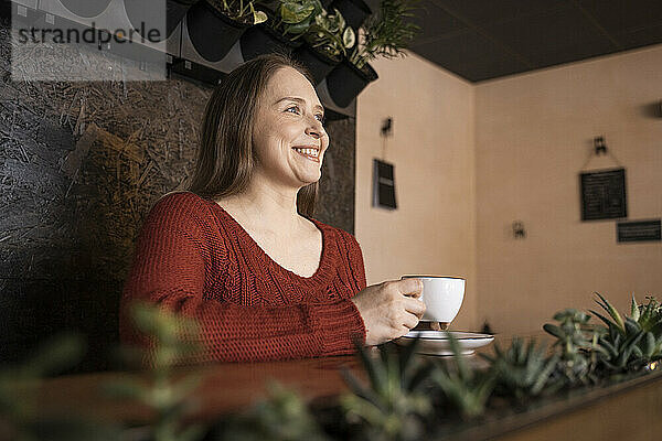 Glückliche Frau mit Kaffeetasse sitzt im Café