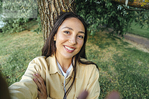 Lächelnde Frau macht ein Selfie vor einem Baum im Park