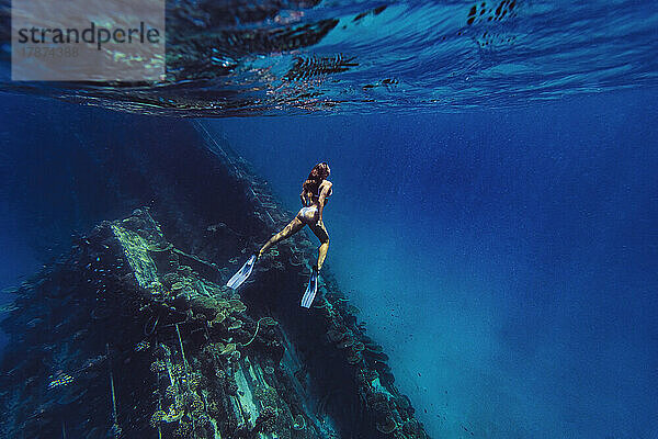 Woman swimming underwater by shipwreck in sea