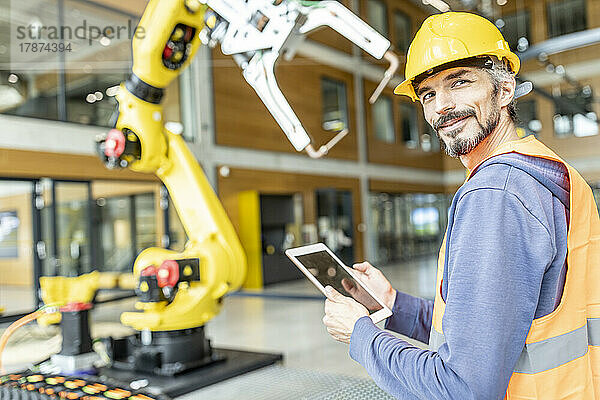Selbstbewusster Facharbeiter steuert Roboterarm mit digitalem Tablet