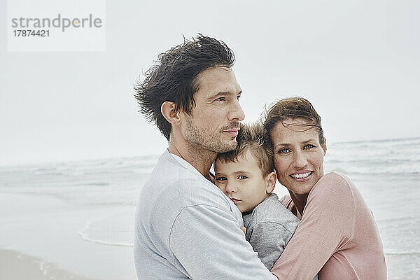 Fürsorgliche Eltern umarmen ihren Sohn am windigen Strand