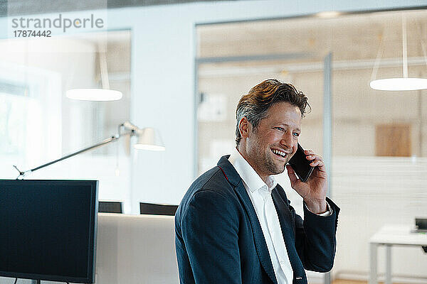 Happy mature businessman talking through mobile phone in office