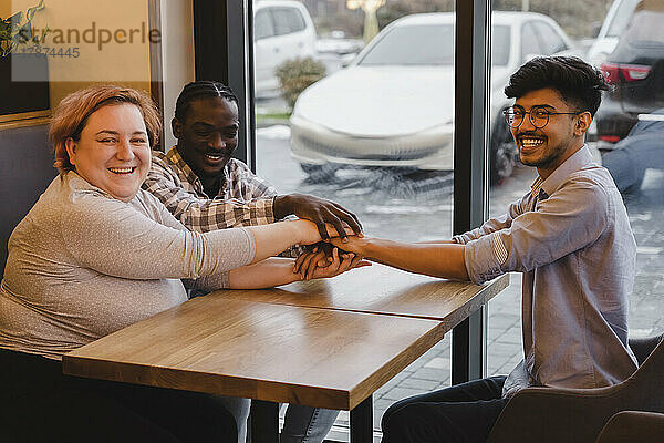 Fröhliche  gemischtrassige Freunde  die sich am Tisch im Café die Hände stapeln