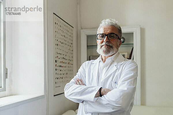 Selbstbewusster Arzt mit Brille und verschränkten Armen in der Klinik