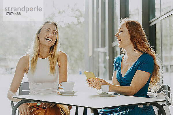 Glückliche Frau mit Smartphone mit Freundin im Straßencafé