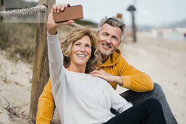Happy mature man with woman taking selfie through mobile phone at beach