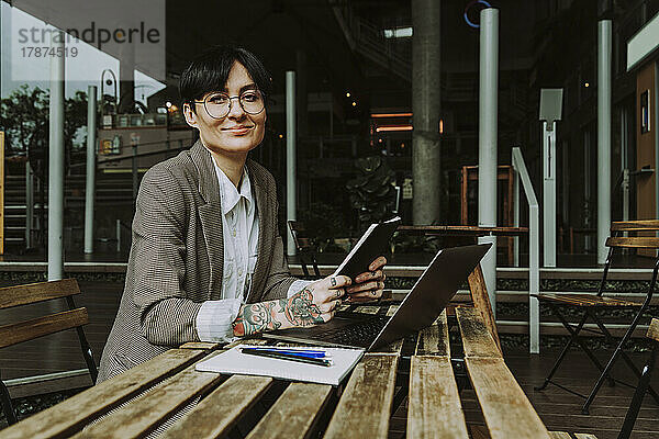 Lächelnde Geschäftsfrau mit Tagebuch und Laptop am Tisch sitzend