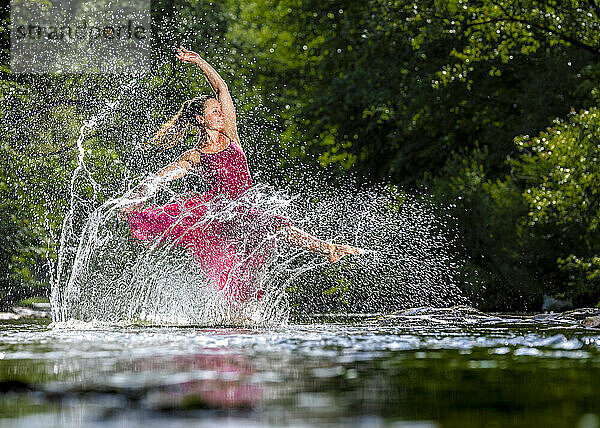 Junge Frau im Kleid spritzt Wasser im Fluss