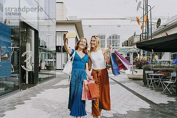 Fröhliche Freunde mit Einkaufstüten machen Selfie mit Smartphone in der Stadt