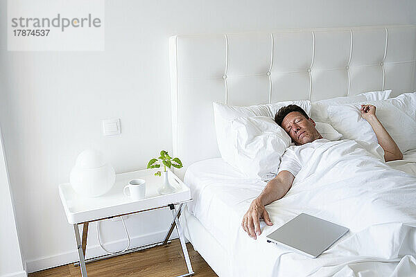Reifer Mann schläft mit Laptop im Bett