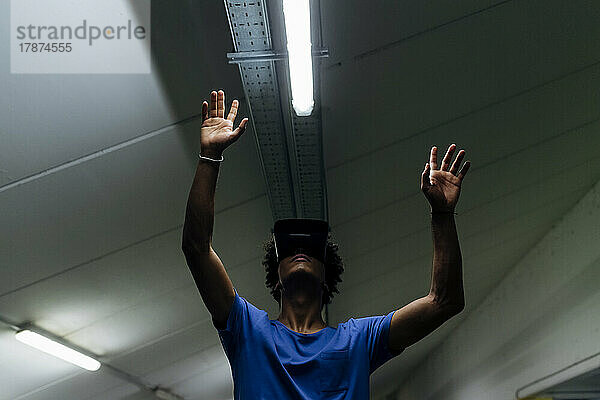 Junger Mann mit erhobenen Armen und Virtual-Reality-Headset in der U-Bahn