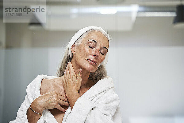 Woman with eyes closed massaging neck in bathroom