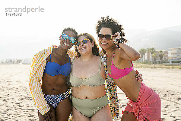 Lächelnde Frauen mit Sonnenbrille und Armen am Strand