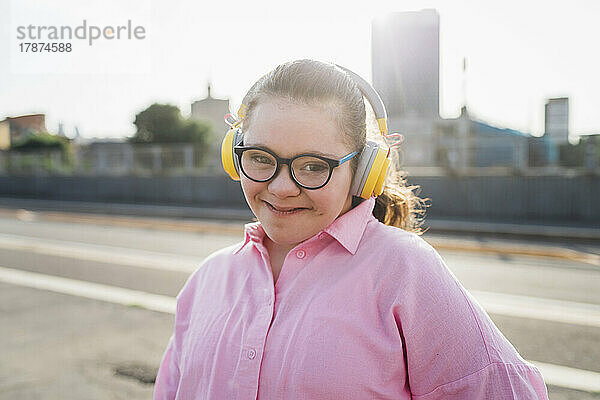 Lächelndes Teenager-Mädchen mit Down-Syndrom  das an einem sonnigen Tag Musik über Kopfhörer hört
