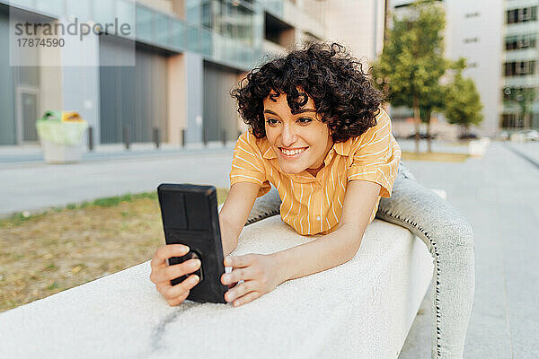 Lächelnde Frau mit Smartphone auf Bank sitzend