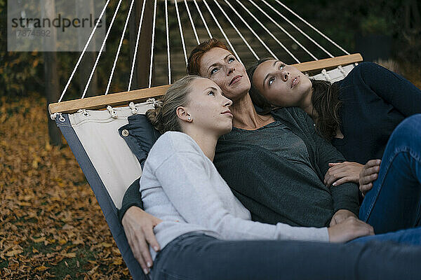 Mutter mit zwei Mädchen im Teenageralter  die im Herbst in der Hängematte im Garten liegen