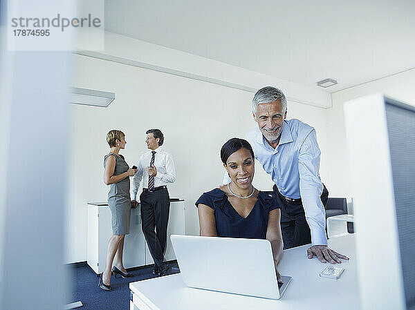 Lächelnde Geschäftsfrau und Geschäftsmann nutzen Laptop mit Kollegen und diskutieren im Büro