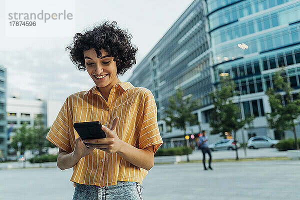 Lächelnde Frau  die vor dem Gebäude ihr Mobiltelefon benutzt