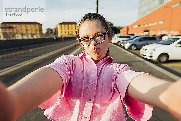 Mädchen mit Down-Syndrom kräuselt sich und macht an einem sonnigen Tag ein Selfie auf der Straße
