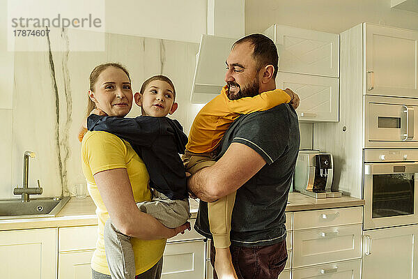 Lächelnde Eltern tragen Söhne in der Küche