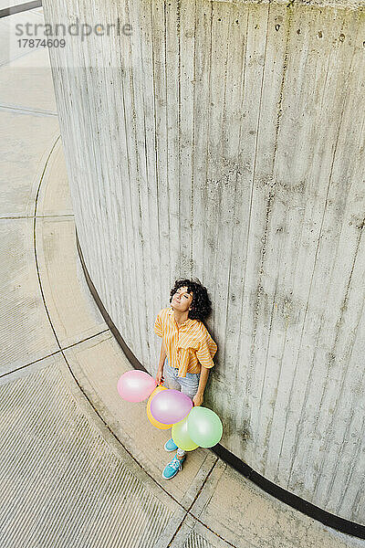 Frau mit bunten Luftballons lehnt an Wand