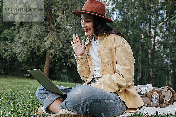 Lächelnde Frau winkt bei Videoanruf über Laptop im Park