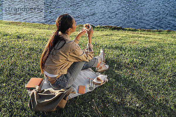 Frau sitzt am See im Park und isst zu Mittag