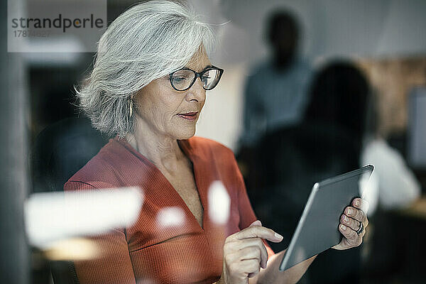 Ältere Geschäftsfrau benutzt Tablet-PC  gesehen durch Glasfenster