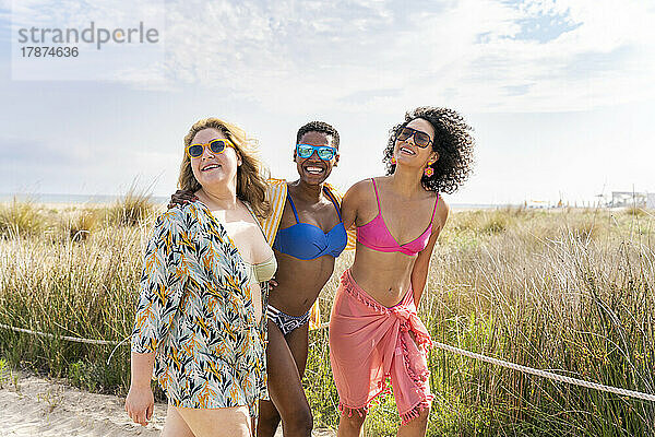 Gemischtrassige Frauen in Bikinis am Strand an einem sonnigen Tag