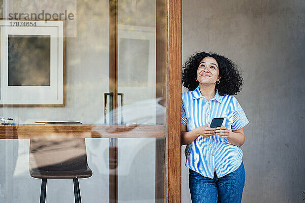 Lächelnde Frau mit Smartphone steht vor der Tür