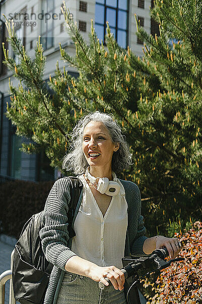 Lächelnde Frau mit Elektroroller an sonnigem Tag